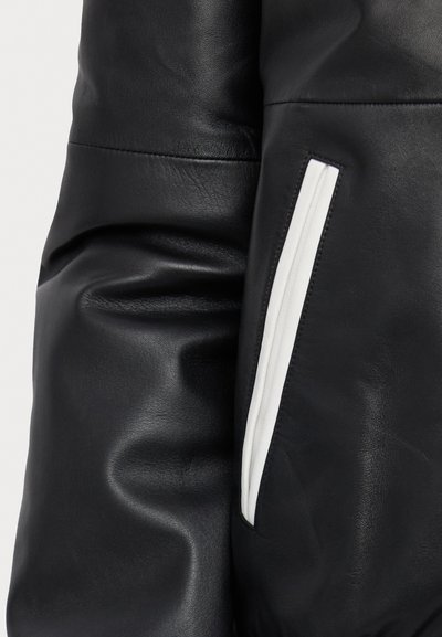 Black leather jacket with a textured finish, featuring a white zippered pocket on the sleeve and a smooth, fitted design.