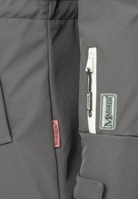 Vêtement d'extérieur gris foncé avec une poche zippée blanche, un patch de marque en caoutchouc et une étiquette rose ; texture lisse avec un design fonctionnel.