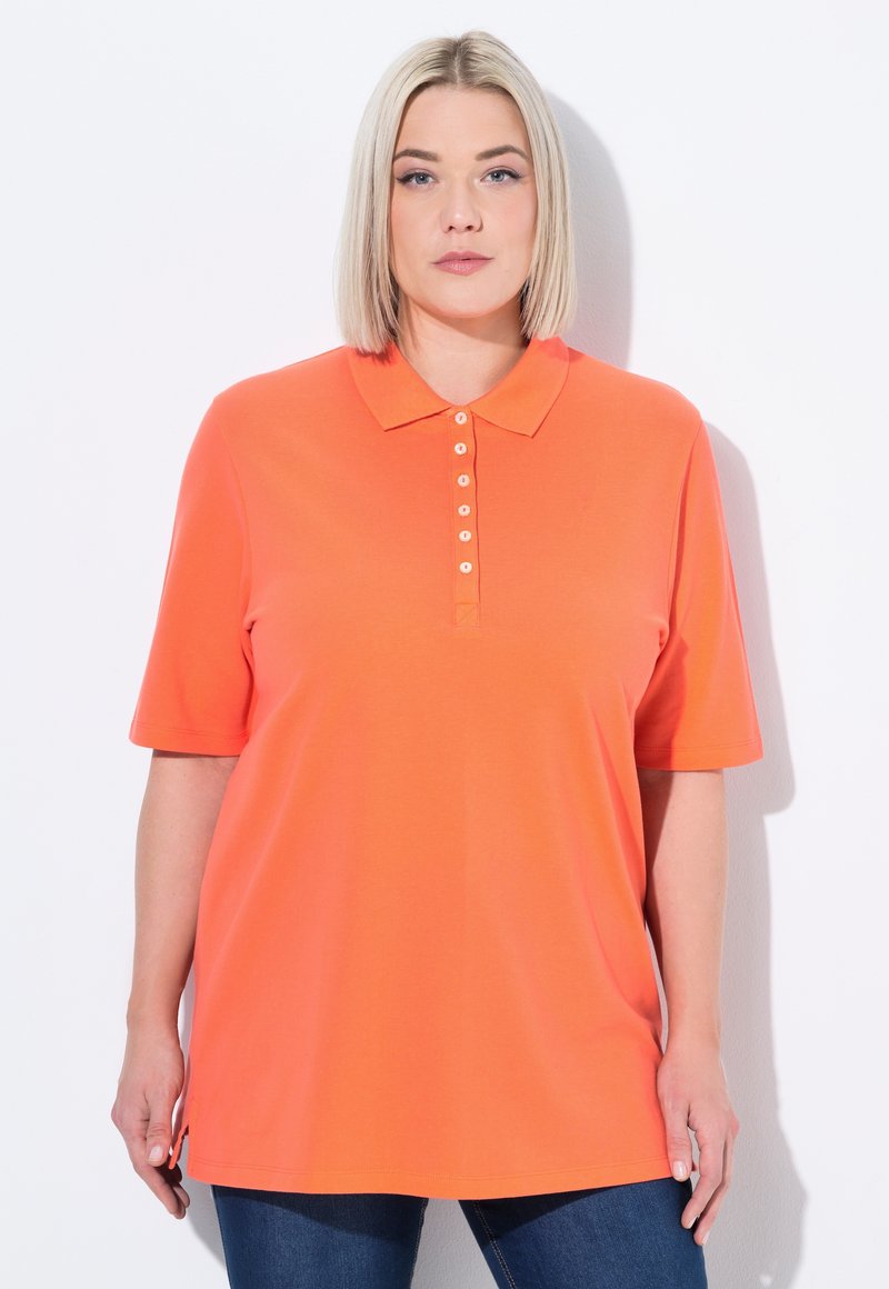 Oranžové polo tričko s krátkým rukávem, s knoflíkovou légou a krémovými knoflíky, a volným střihem, spárované s tmavě modrými džínami.