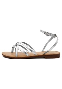 Sandalo strappy argento metallico con suola piatta color tortora, caratterizzato da multiple cinture incrociate e una fibbia regolabile alla caviglia.