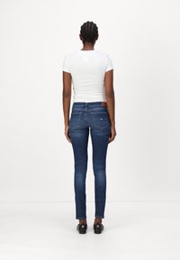 Jeans blu in denim slim-fit con vita media, tasche posteriori e una toppa in pelle marrone in vita, abbinati a una t-shirt bianca aderente.