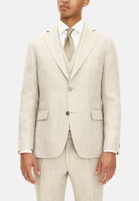 Beige linnekostym med en enkelspårig jacka, slagkragar, två framfickor och matchande byxor. Mönstrad slips kompletterar helheten.