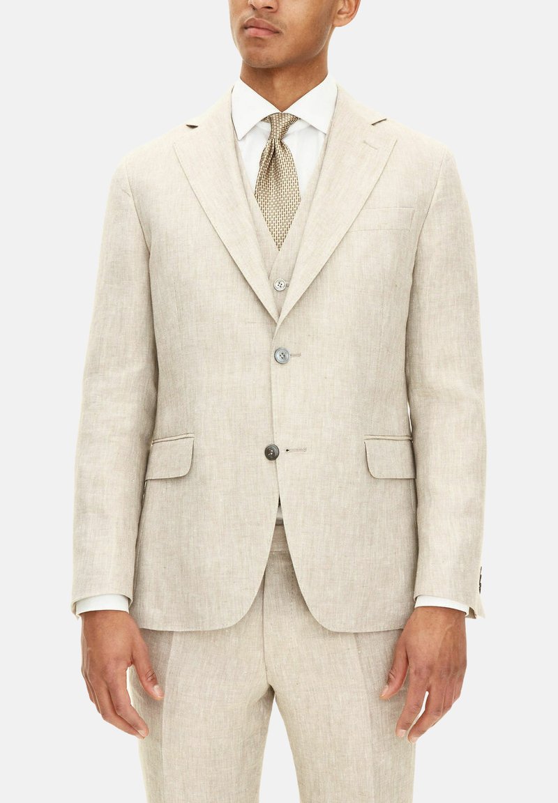 Beige linnekostym med en enkelspårig jacka, slagkragar, två framfickor och matchande byxor. Mönstrad slips kompletterar helheten.