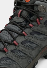 Gray hiking shoe with mesh and suede materials, featuring red accents and durable rubber soles. Prominent lacing system and textured surfaces.
