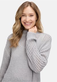Hellgrauer, locker gestrickter Pullover mit hohem Halsausschnitt und gerippten Bündchen. Hat eine offene Strickstruktur, die einen lässigen Look verleiht.