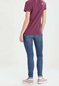 Lyhythihainen viininpunainen t-paita, siniset kapeat farkut ja vaaleanpunaiset lenkkarit. Yksinkertainen muotoilu, pehmeä rakenne ja logodetaili takana.