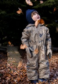 Beige waterdichte skipak met dierenpatronen, elastische manchetten en aangehechte wanten. Het kind draagt een blauwe gebreide muts en wordt omringd door vallende bladeren.