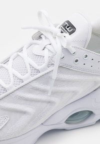 Scarpa da ginnastica bianca con tomaia in rete, sovrapposizioni sintetiche testurizzate, design con lacci e ammortizzazione d'aria visibile nella suola.