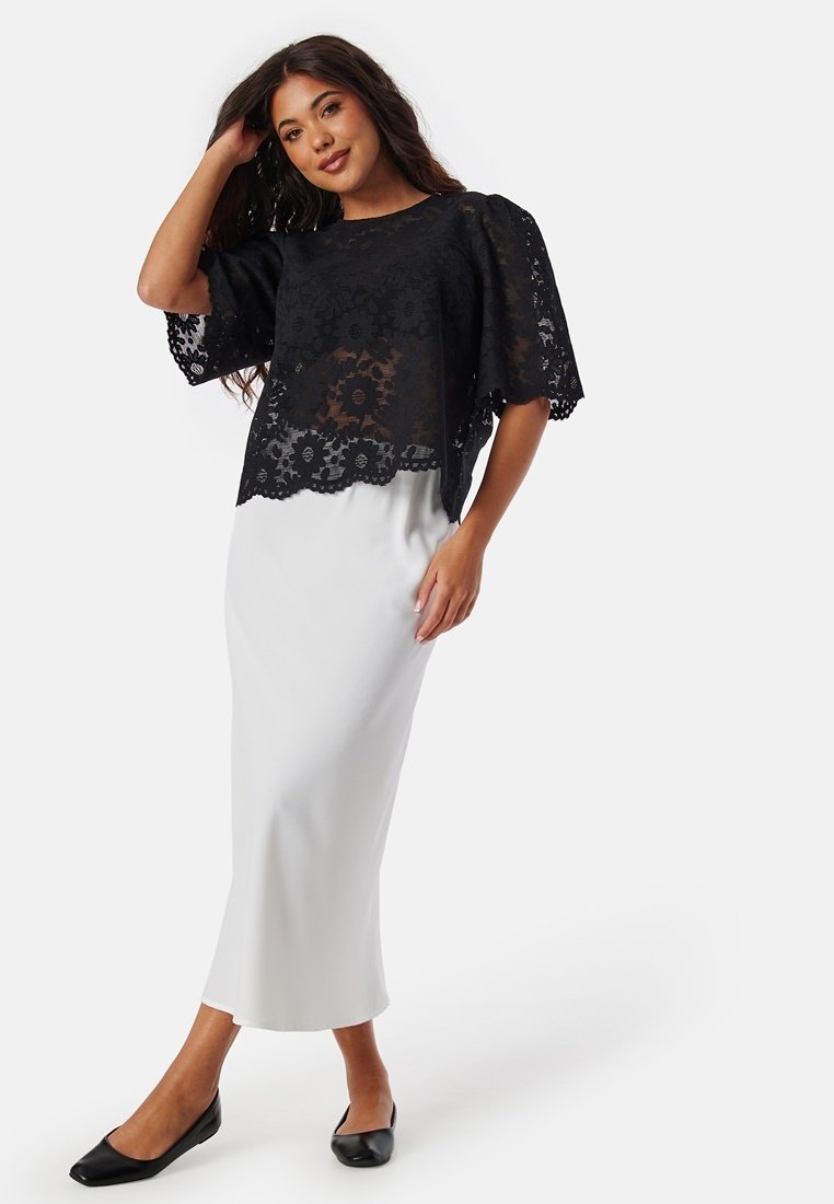 Zwarte kanten top met korte mouwen, gelaagd over een gladde witte maxi rok. Zwarte flats maken de outfit compleet.