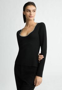 Top nero a maniche lunghe con scollatura profonda a girocollo, accentuato da un bordo metallico. Tessuto in maglia morbida, design aderente e texture liscia.