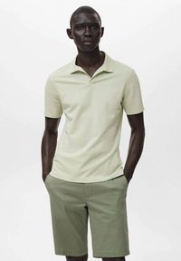 Světle zelené polo tričko s krátkým límečkem, spárované s olivově zelenými šortkami. Hladký materiál a klasický design.