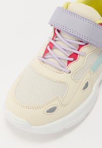 Gaiši bežs skrējiens ar sietiņa un sintētiskām pārklājumiem. Krāsas akcenti sarkanā un zilā krāsā, satur purpura velcro siksnu un teksturētu zoli.