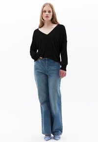 Top a maniche lunghe nera con scollatura a V abbinato a jeans a gamba larga azzurri. L'outfit presenta una vestibilità comoda e polsini a coste, con tacchi blu.