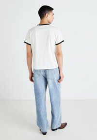 T-shirt blanc avec des finitions noires, associé à un jean large bleu clair. Le T-shirt présente un col rond et des manches courtes, le tissu est doux.
