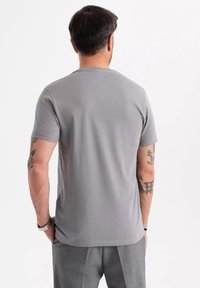 T-shirt grigio a maniche corte in tessuto morbido, con scollatura a girocollo. La vista posteriore mostra una texture liscia, senza motivi o loghi visibili.