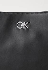 Borsa a tracolla in pelle nera con un accentuato logo argento. La trama è liscia con lievi dettagli superficiali.