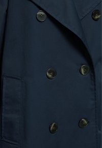 Cappotto doppiopetto blu scuro con sei bottoni neri e una tasca laterale, che mostra un rever piegato e una texture liscia del tessuto.