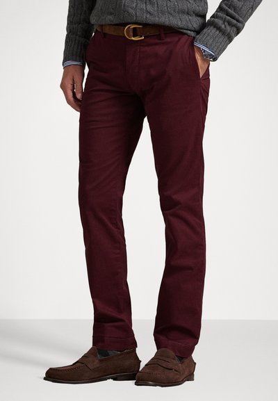 Bordeauxfarbene Chinos aus Baumwolle, mit schmaler Passform, seitlichen Taschen und einem braunen Ledergürtel. Kombination mit braunen Wildlederschlüpfschuhen.