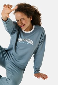 Hellblaues Sweatshirt mit weißem Kragen, versehen mit dem Aufdruck "COSY VIBES". Kombiniert mit passenden hellblauen Hosen, weich und lässig geschnitten.