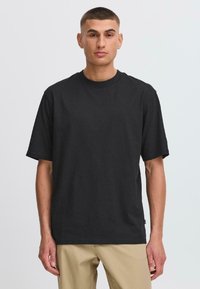 T-shirt noir à manches courtes en coton, avec un col rond, une coupe décontractée et un design minimaliste sans motifs ni accents visibles.