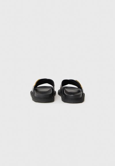 Svarta sandaler med två breda remmar, platt sula och en slät textur. Har en guldaccent på remmen och en minimalistisk design.
