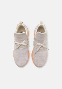 Scarpe da atletica color beige chiaro con una tomaia in maglia testurizzata, lacci elastici e suola in gomma arancione. Nome del marchio "ARKK" impresso sul tallone.