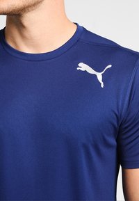Námořnická modrá sportovní tričko s kulatým výstřihem, hladkou texturou, krátkými rukávy a bílým logem Puma na levém horním prsu.