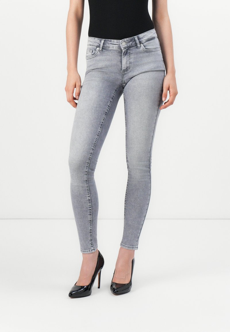 Grå skinny jeans laget av denim, med klassisk fem-lomme design og subtil fading, kombinert med svarte høye hæler.