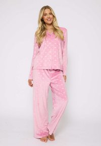 Conjunto de pijama rosa hecho de tela suave; la parte superior cuenta con un diseño de botones con cuello, y los pantalones tienen un ajuste relajado, ambos adornados con pequeños patrones de corazones.