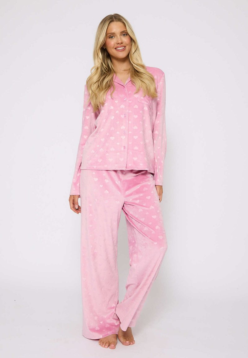 Conjunto de pijama rosa hecho de tela suave; la parte superior cuenta con un diseño de botones con cuello, y los pantalones tienen un ajuste relajado, ambos adornados con pequeños patrones de corazones.