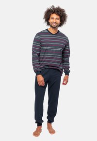 Långärmad mörkgrå V-ringad tröja med horisontella randiga mönster i vitt och rosa. Ett par marinblå byxor med elastiska muddar, barfota.