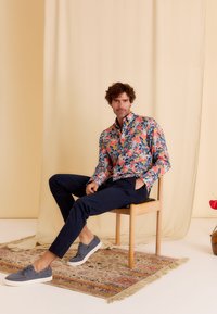 Langarmshirt met bloemenpatroon in marineblauw, met kleurrijke bloemen. Een paar marineblauwe broeken en grijze casual schoenen maken de outfit compleet.