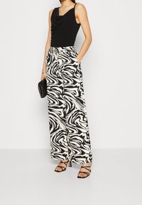 Svart ärmlös topp med draperad halsringning, i kombination med vida byxor med ett svart och vitt virvlande mönster. Svarta klackar med remmar.