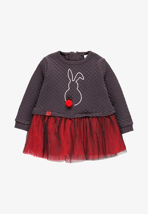 Top acolchado de color gris oscuro con mangas largas, que presenta un contorno de conejo blanco y un acento de pom-pom rojo; falda de tul roja en varias capas con forro negro.