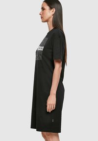 Czarna bawełniana sukienka t-shirtowa z krótkim rękawem, luźnym krojem i grafiką na piersi. Gładka tekstura i długość do kolan.