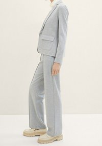 Lichtgrijs, op maat gemaakt pak met een fitted blazer en wijde broekspijpen, gemaakt van een gladde, textuurstof. Chunky beige schoenen maken de look compleet.