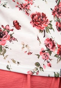 Tissu à motif floral dans des nuances de rose, rouge et vert, superposé sur un fond en corail uni. Texture douce avec un tombé léger.