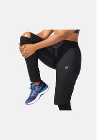 Zwarte sportbroek met een aansluitend ontwerp beschikt over een zijvak met rits. Gecombineerd met blauwe en roze hardloopschoenen, die een gestructureerde bovenkant benadrukken.