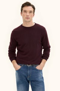 Burgunderfarbener Rundhalspullover mit langenÄrmeln, kombiniert mit blauen Jeans. Der Pulloverstoff wirkt glatt; die Jeans haben Standardtaschen und Nahtdetails.