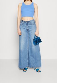 Un crop top bleu clair associé à un jean évasé en délavé clair. Les accessoires comprennent un petit sac à main bleu brillant et des sandales à talons bleues.