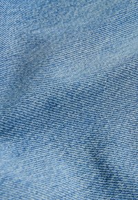 Gros plan d'un tissu denim bleu clair montrant une texture de tissage diagonal et des plis subtils.