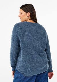 Maglione lavorato a maglia in blu melange, con scollatura rotonda, maniche lunghe e texture a coste. Orlo posteriore leggermente più lungo.