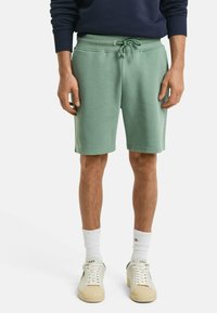 Shorts en coton vert clair avec une taille élastique et un cordon de serrage. Associés à des chaussettes blanches et des baskets beiges. Design simple et décontracté.