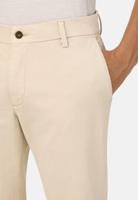 Šviesiai rudos spalvos tiesaus kirpimo kelnės, su mygtuko uzdarymu ir šoninėmis kišenėmis; pagamintos iš tekstūruoto audinio. Diržo kilpa matoma ant juosmens.