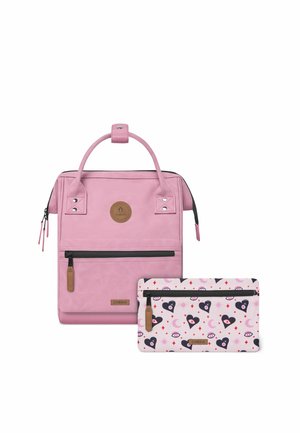 Pink backpack with a smooth texture, featuring a top handle, front zip pocket, and a logo patch. Accompanied by a patterned pink accessory pouch.