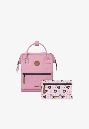 Pink backpack with a smooth texture, featuring a top handle, front zip pocket, and a logo patch. Accompanied by a patterned pink accessory pouch.