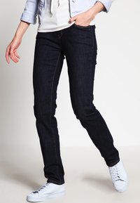 Mörkblå denimjeans med slim fit, subtil kontrastsöm och framfickor, parat med vita sneakers och en lätt jacka.