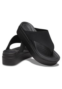 Sandali Crocs neri con suola ampia e piatta, design a infradito e cinturino testurizzato. Presentano una soletta imbottita e un sottile dettaglio del logo.