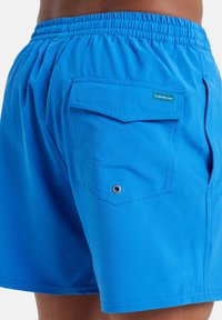 Modré plážové šortky vyrobené z ľahkej tkaniny, s elastickým pásom, zadnou vreckom so chlopňou a detailom z kovového očká.