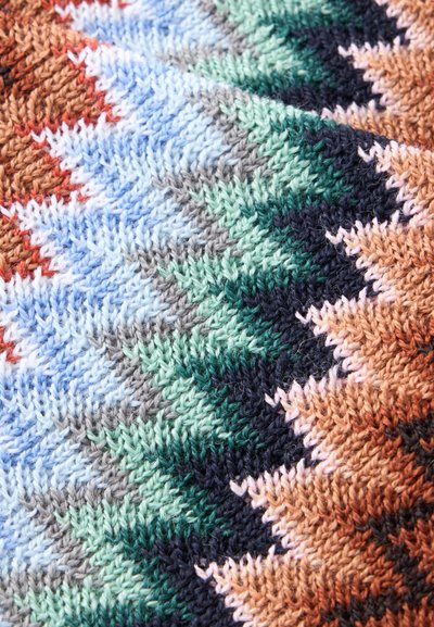 Gros plan d'un tissu tricoté multicolore avec des motifs en zigzag dans des tons bleus, verts, marron, orange et gris.